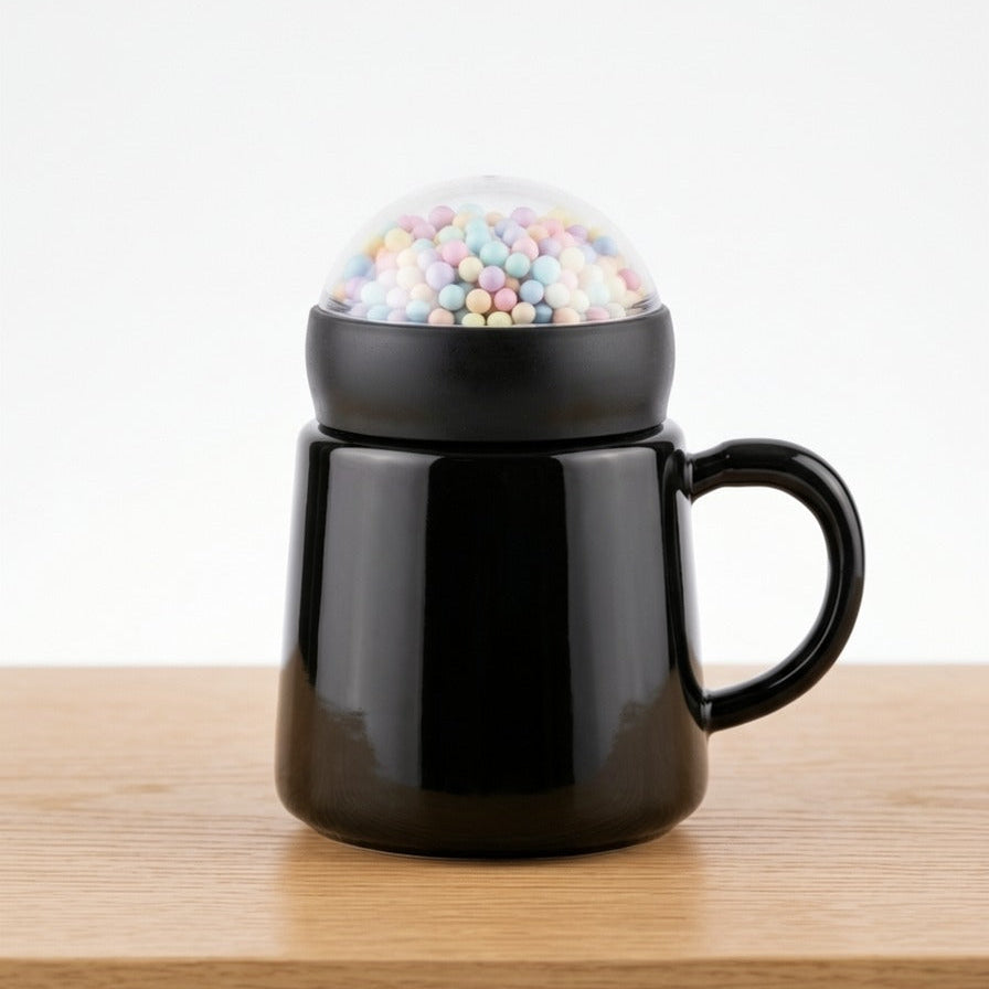 A modern glossy black ceramic mug by Gift by Hamza with a unique transparent dome lid filled with colorful pastel mini spheres.