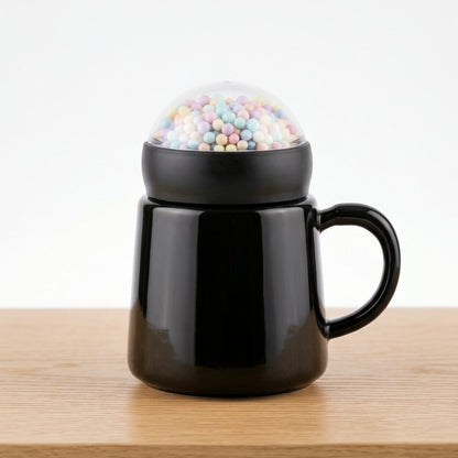 A modern glossy black ceramic mug by Gift by Hamza with a unique transparent dome lid filled with colorful pastel mini spheres.