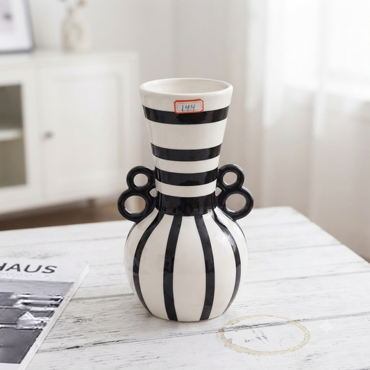 Black and white striped ceramic decorative vase with dual ring handles on a white marble surface.