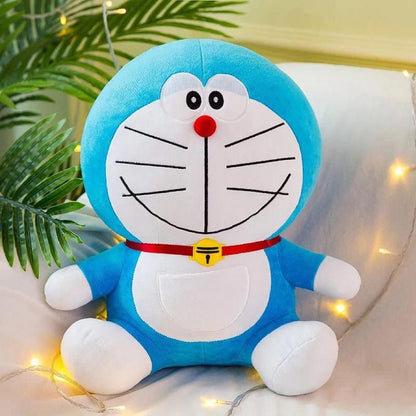 Cute blue and white Doraemon soft plush toy with red collar and yellow bell sitting against a decorated background.