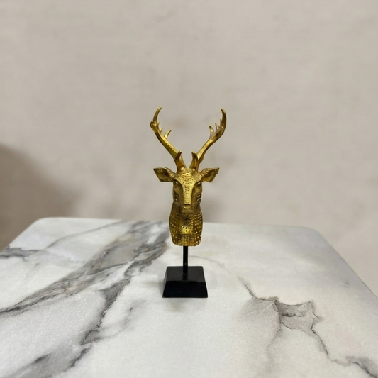 Golden geometric deer head figurine with majestic antlers mounted on a black stand against a light background.