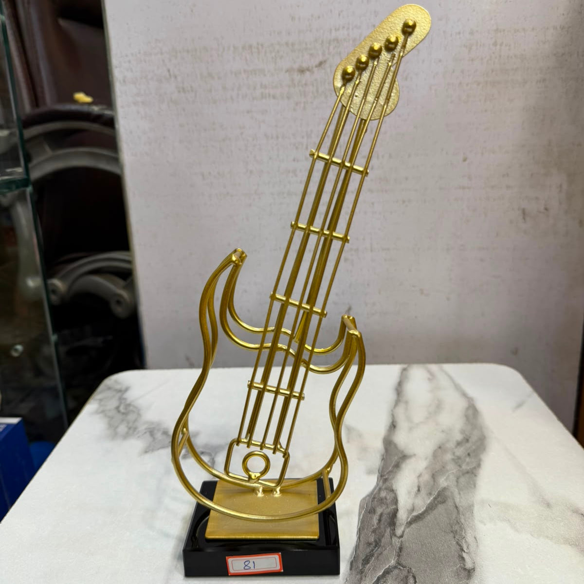 A minimalist gold-toned metal electric guitar showpiece by Gift by Hamza with a sleek black base, perfect for modern home decor.