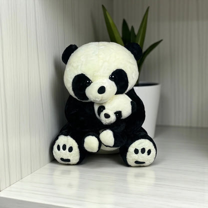 A soft, cute mother and baby panda plush toy sitting together against a light background with a decorative plant in a white pot.