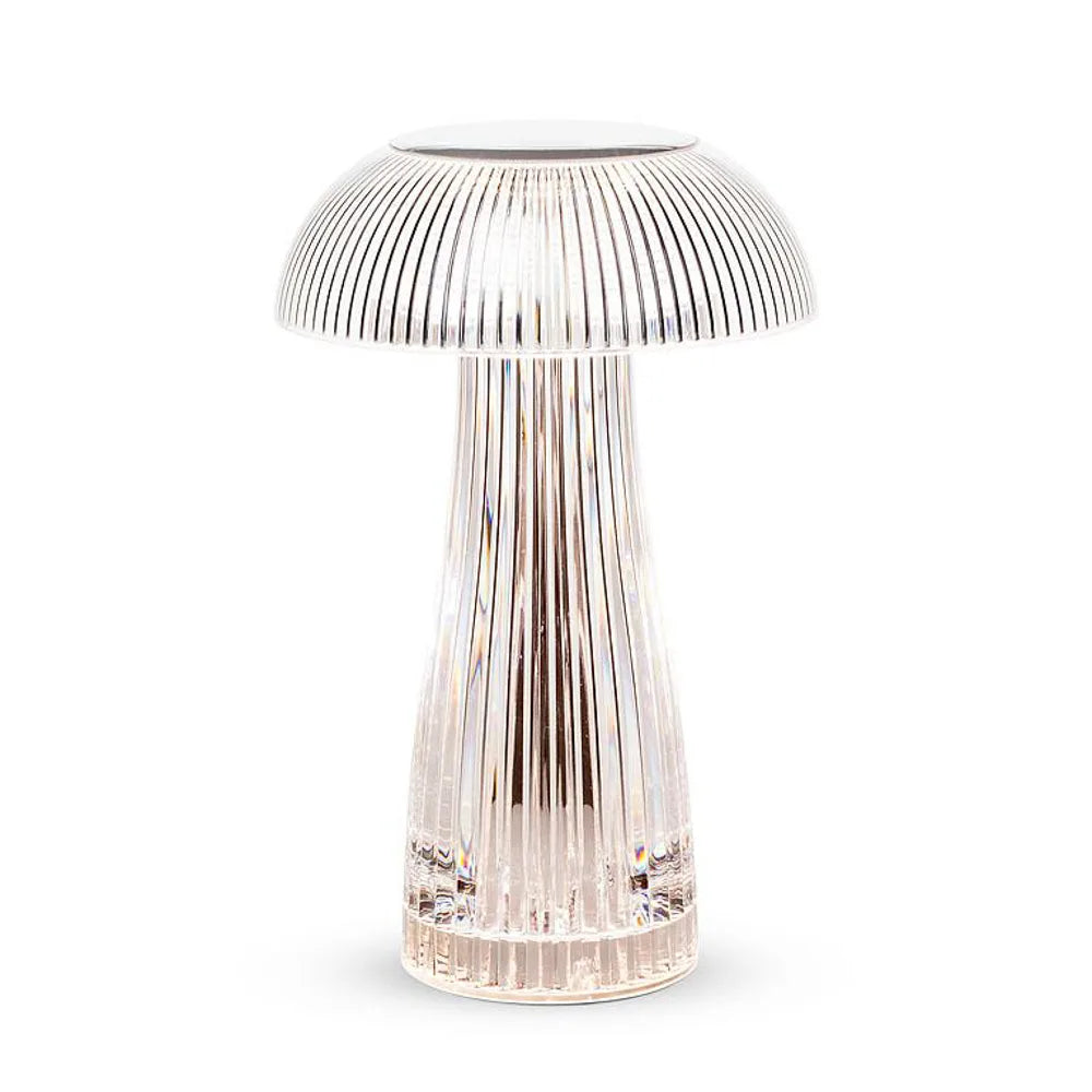 Modern transparent acrylic mushroom table lamp on a grey surface next to a white mug and a stack of colorful notebooks.