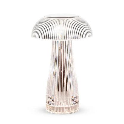 Modern transparent acrylic mushroom table lamp on a grey surface next to a white mug and a stack of colorful notebooks.