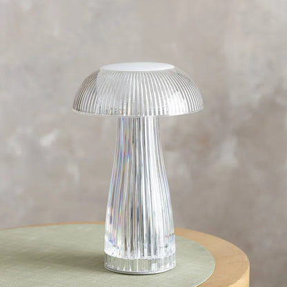 Modern transparent acrylic mushroom table lamp on a grey surface next to a white mug and a stack of colorful notebooks.