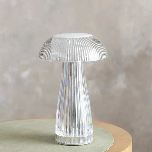 Modern transparent acrylic mushroom table lamp on a grey surface next to a white mug and a stack of colorful notebooks.